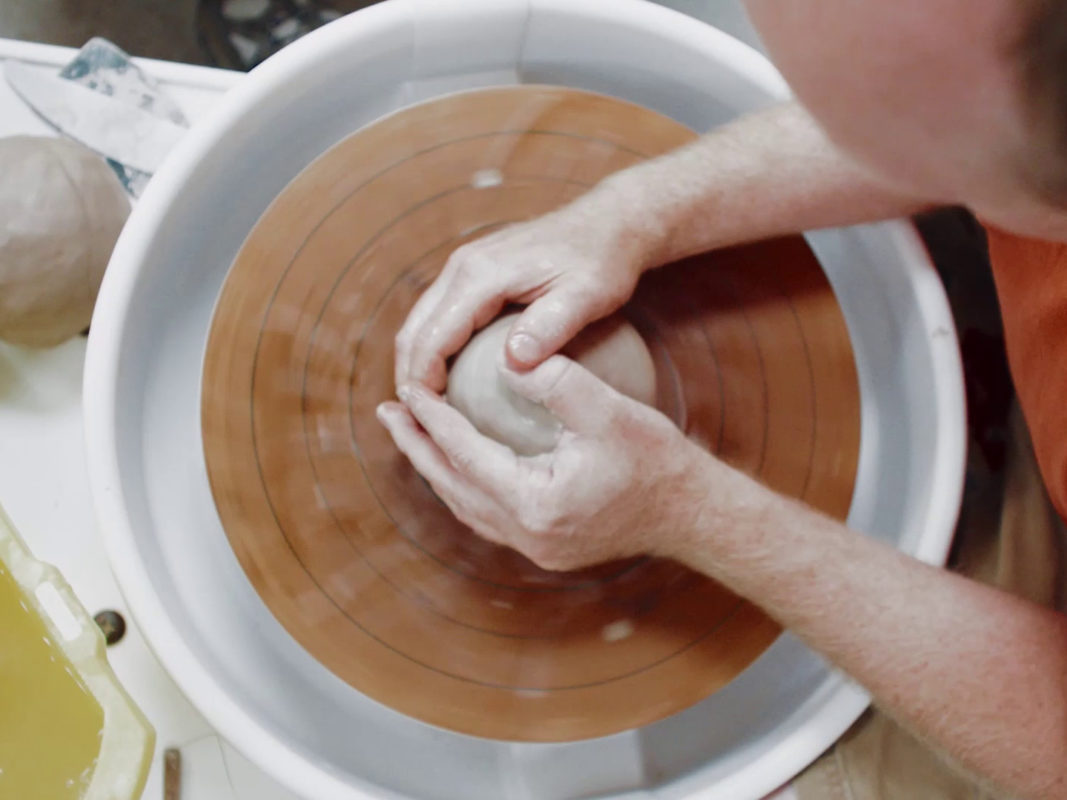 Close-up photo of two hands forming clay spinning on a pottery wheel.