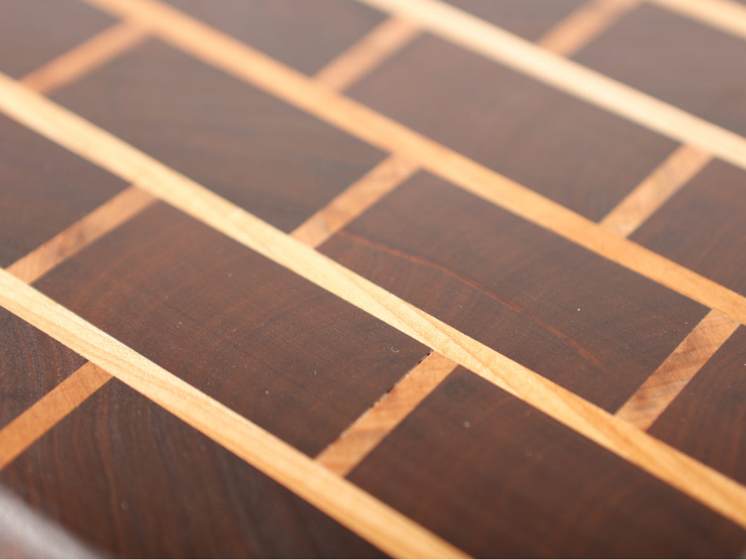 Close-up photo of a wooden cutting board with a rectangular checkerboard pattern.