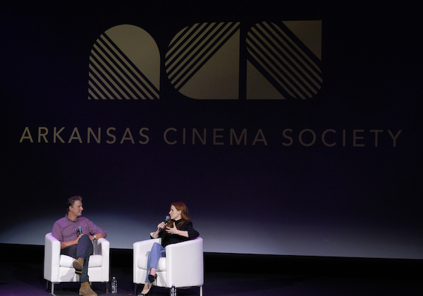 Photo of Arkansas Cinema Society Co-Founder Jeff Nichols and actress/producer Jessica Chastain sitting on white chairs and holding microphones on a stage. Behind them, a projected image reads "Arkansas Cinema Society."