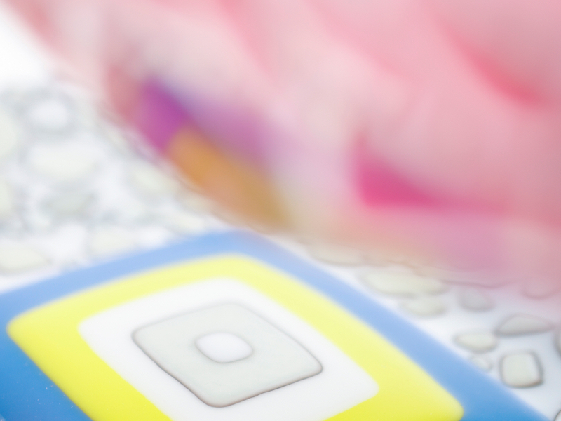 Close up photo of handmade glass objects. The full objects are partially blurred, showing abstracted streaks of pink, red, blue, yellow, and white glass.