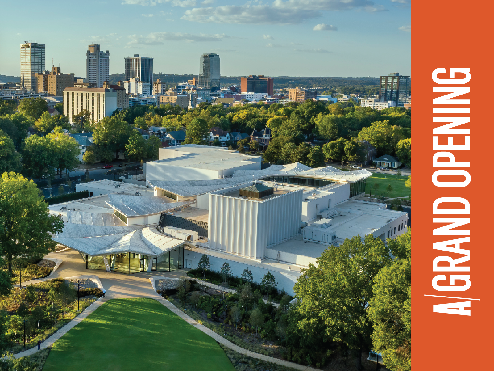 An aerial photo of the Arkansas Museum of Fine Arts viewed from the south with the Downtown Little Rock skyline visible in the background. On the right side of the photo, there is an orange bar with white letters on top reading "A Grand Opening."