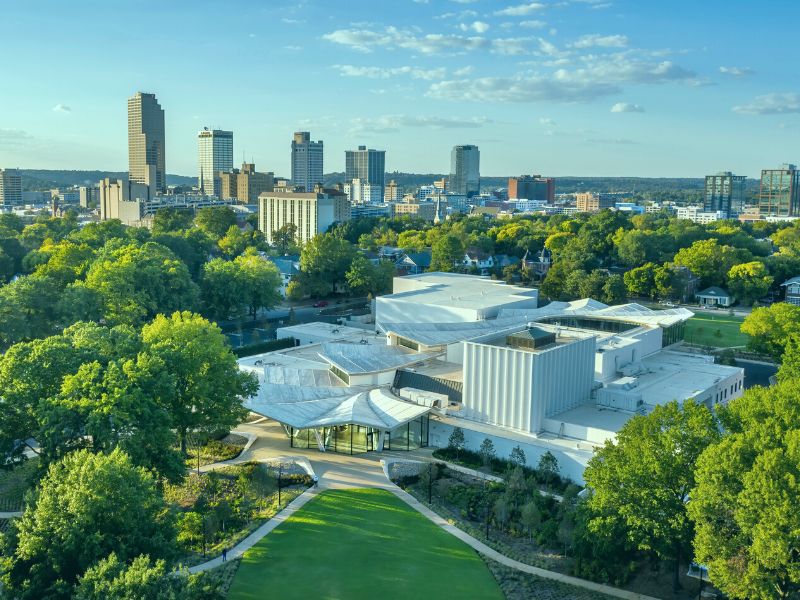Aerial photo of the Arkansas Museum of Fine Arts viewed from the south side of MacArthur Park with the Little Rock skyline visible in the background.