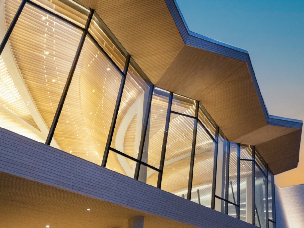 A nighttime photo looking up at the glass windows and angled roofline of AMFA's Cultural Living Room.