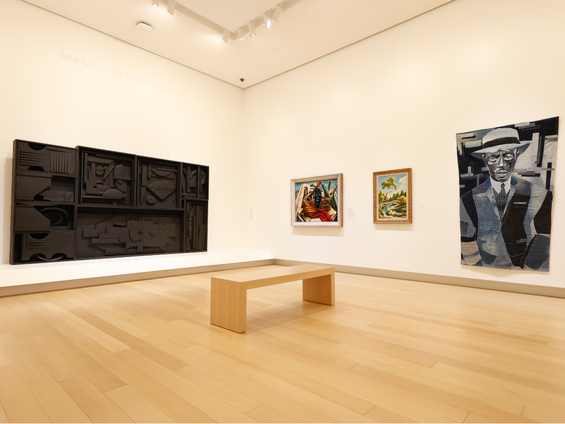 Photo of an art gallery with a bench in the middle of the room.
