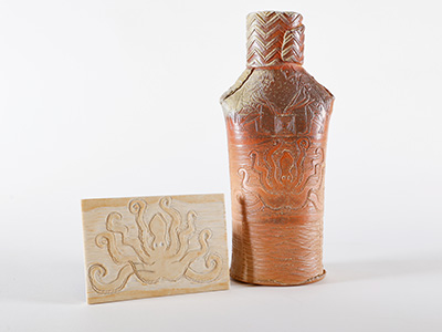 Photo of a clay vase and a small rectangular printmaking block depicting an octupus.