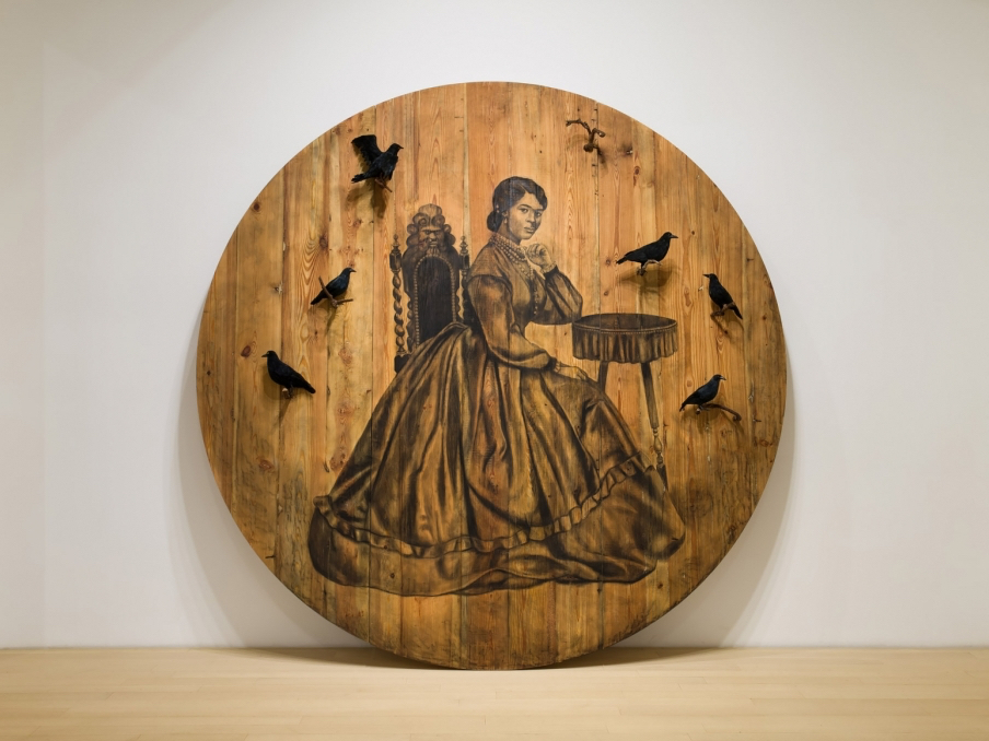 Photo of a large, round slab of wood with a black drawing of a seated woman surrounded by black birds.