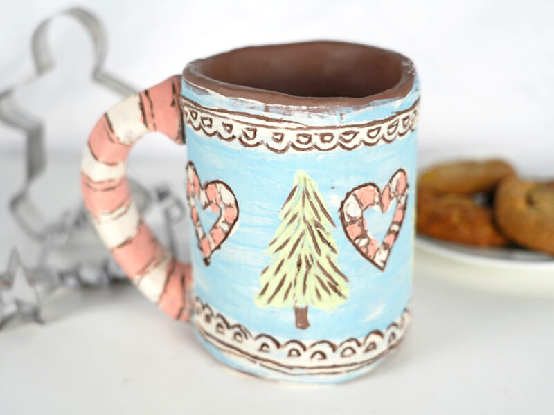 Photo of a handmade ceramic mug painting with hearts and a Christmas tree.