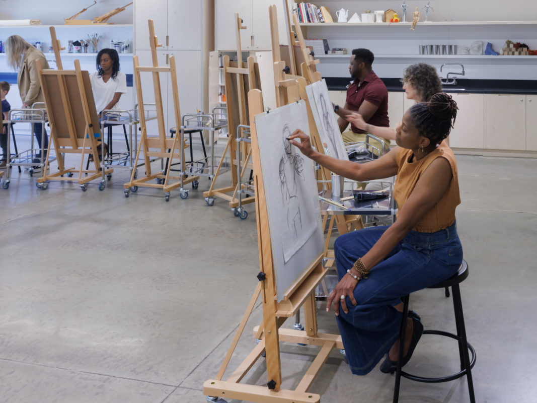 Photo of a group of adults sitting and drawing on easels in an art studio.