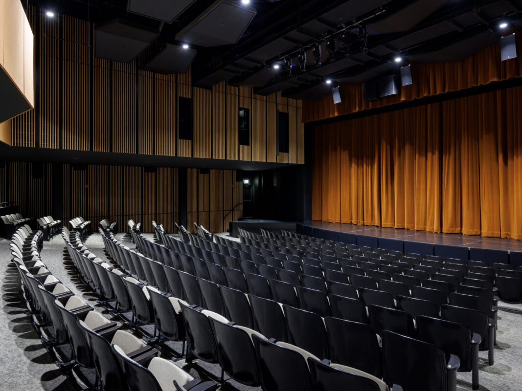 Photo of the Performing Arts Theater at the Arkansas Museum of Fine Arts showing empty black theater seats and a closed golden yellow stage curtain.