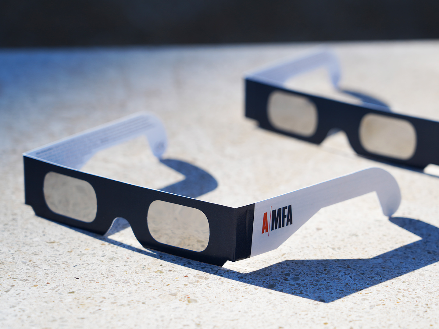 Photo of AMFA-branded eclipse glasses on a stone surface.