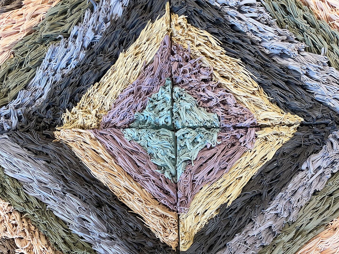 Close-up photo of a ceramic sculpture by Risa Hricovsky that looks like a pastel-colored patterned shag rug.