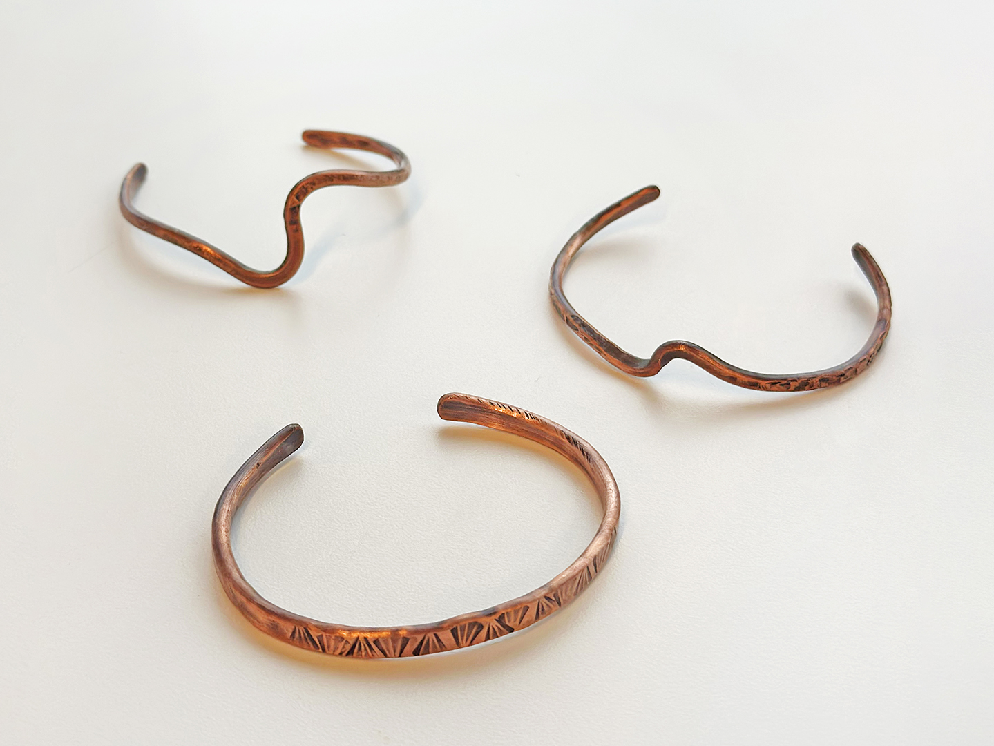 Photo of three handmade copper cuff in unique shapes and designs.