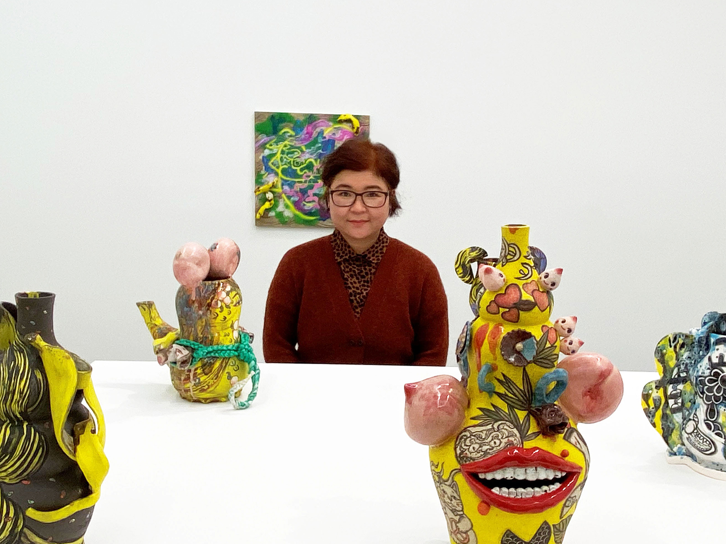 Photo of Jiha Moon standing in an art gallery next to a few of a her sculptures on a white platform.