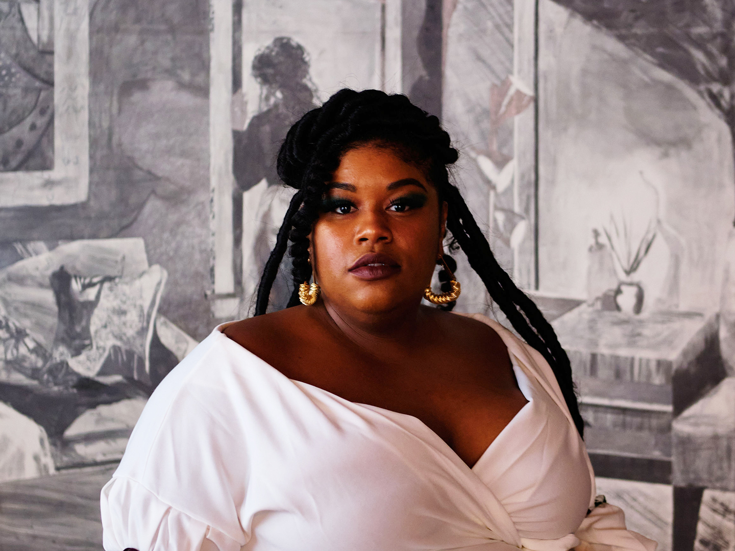 Photo of Glyneisah Johnson wearing a white blouse and gold hoop earrings standing in front of one of her paintings.