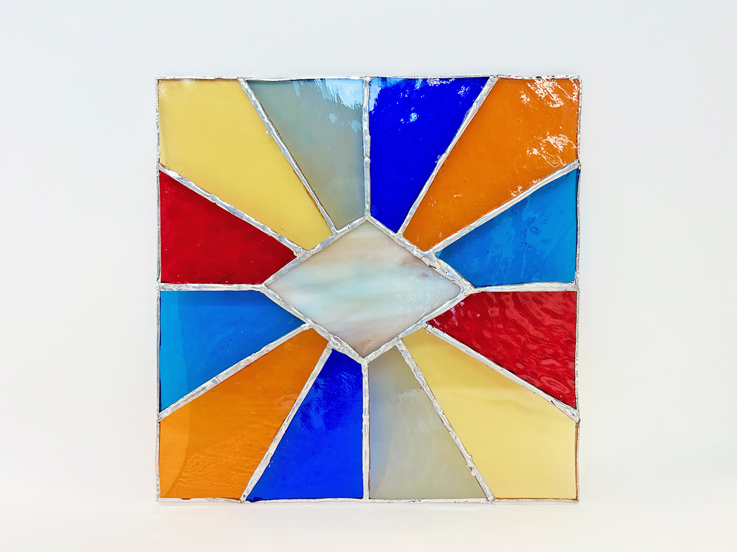 Photo of a square stained glass suncatcher with a starburst pattern.