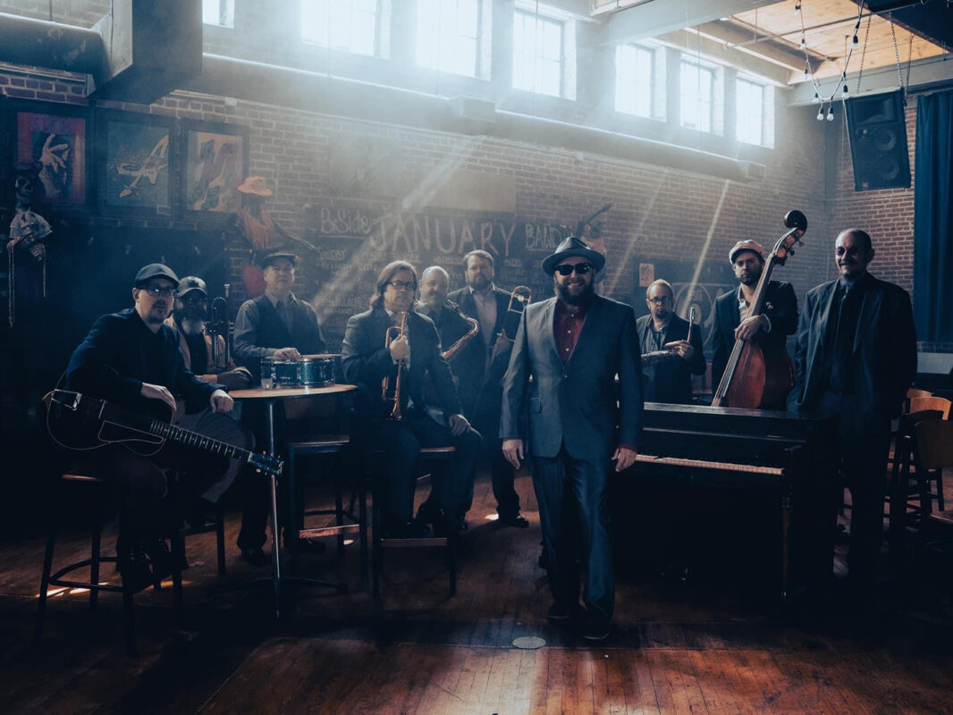 Photo of 10 men holding various instruments posed in a bar in front of a small stage.