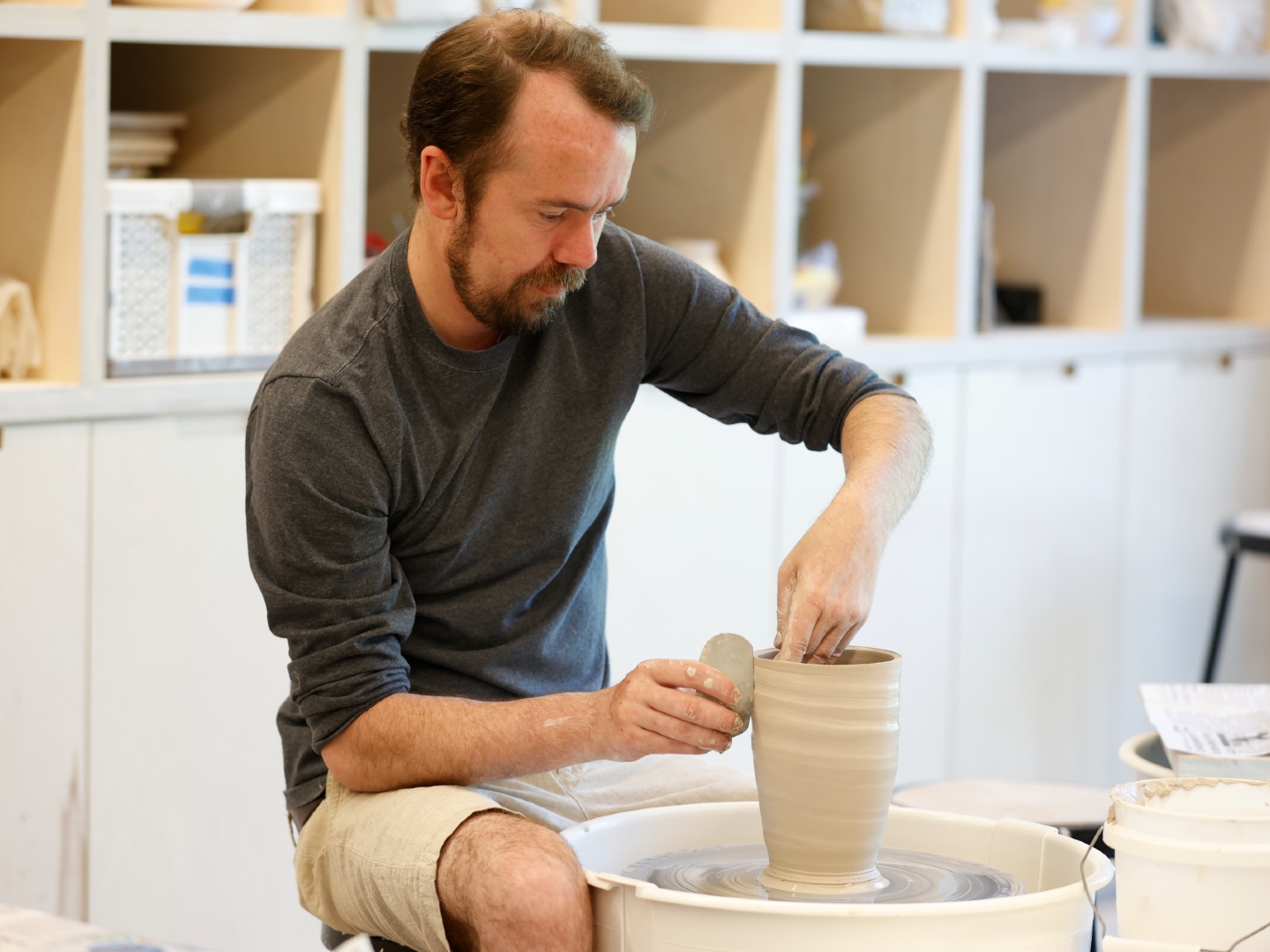 Photo of a man making a vase on a pottery wheel in an art studio.