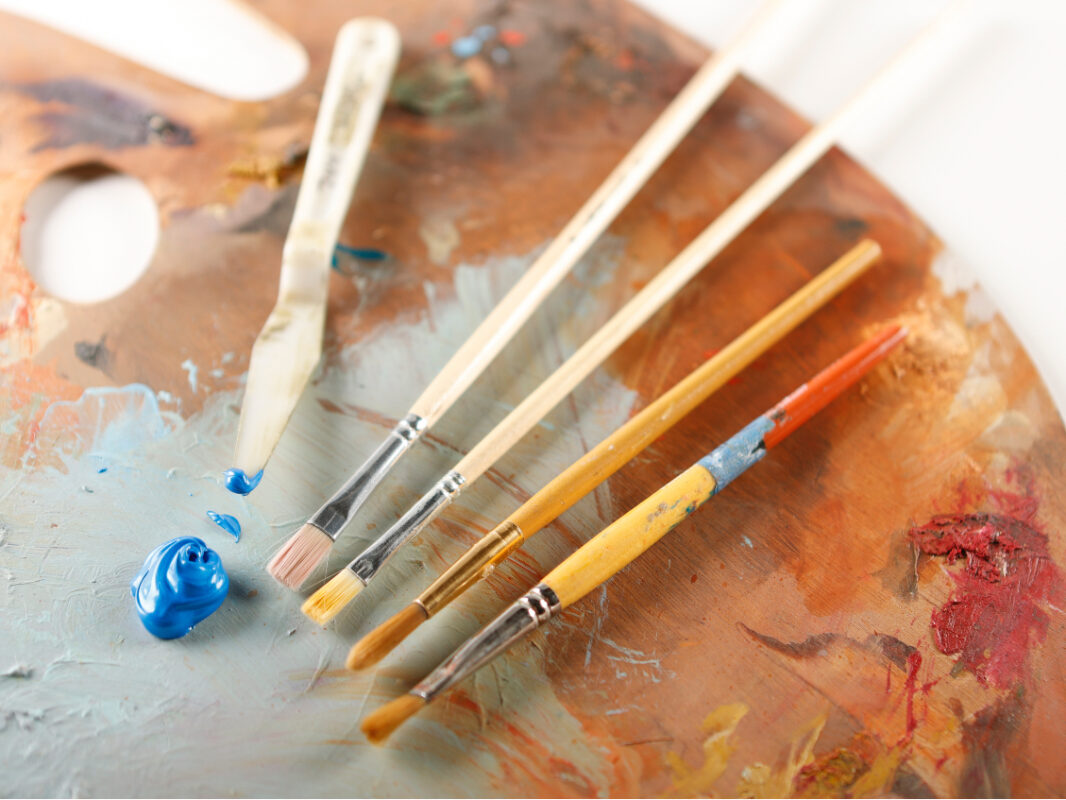 Photo of several paintbrushes and a dollop of blue paint laying on an artist palette.