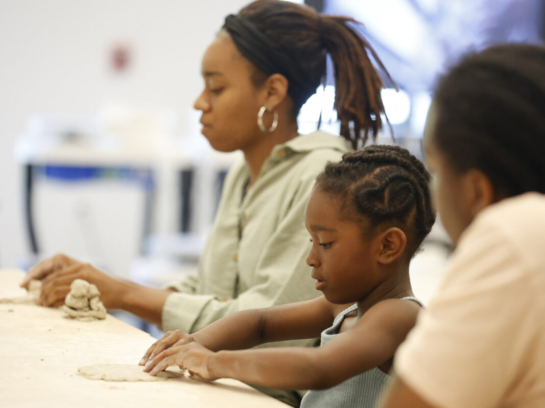 Photo of a woman and a young girl hand building something with clay on a table in an art studio.