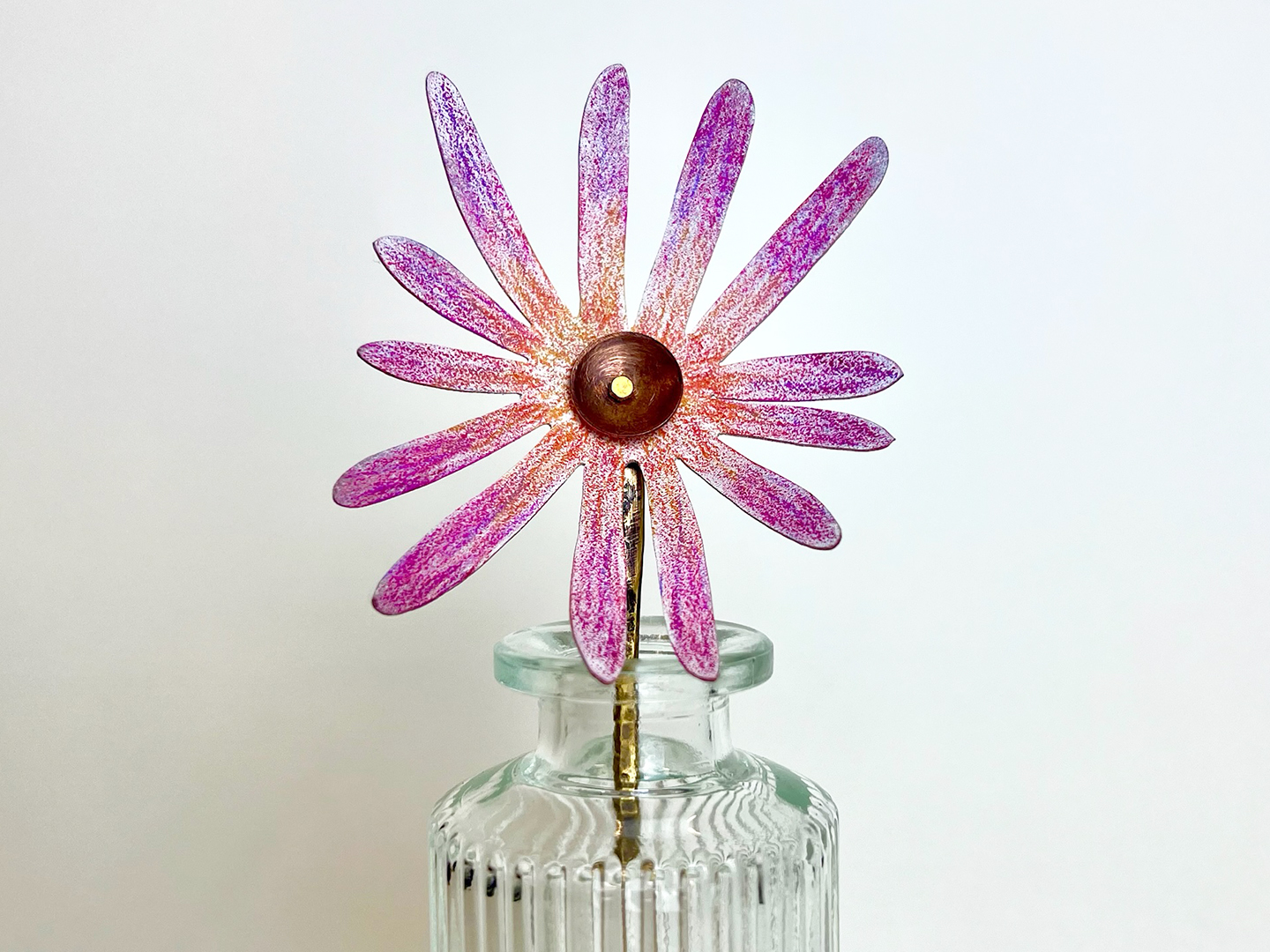 Photo of a metal flower with pink and purple petals sitting in a small glass vase.