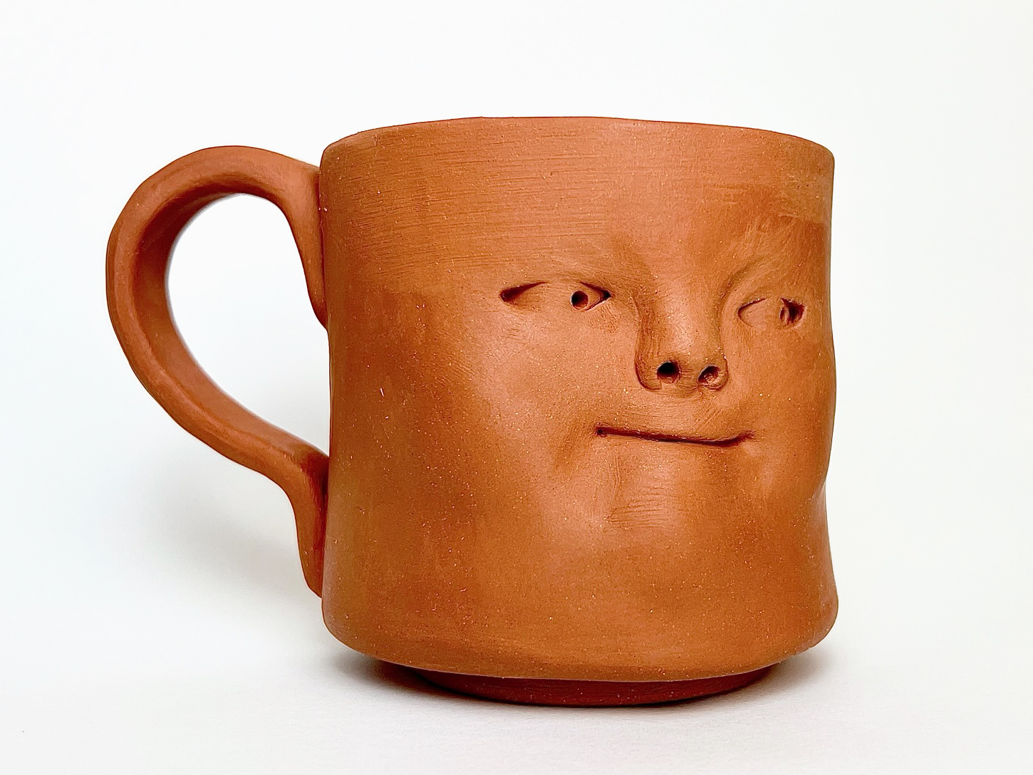 Photo of a clay mug decorated by a sculpted face.