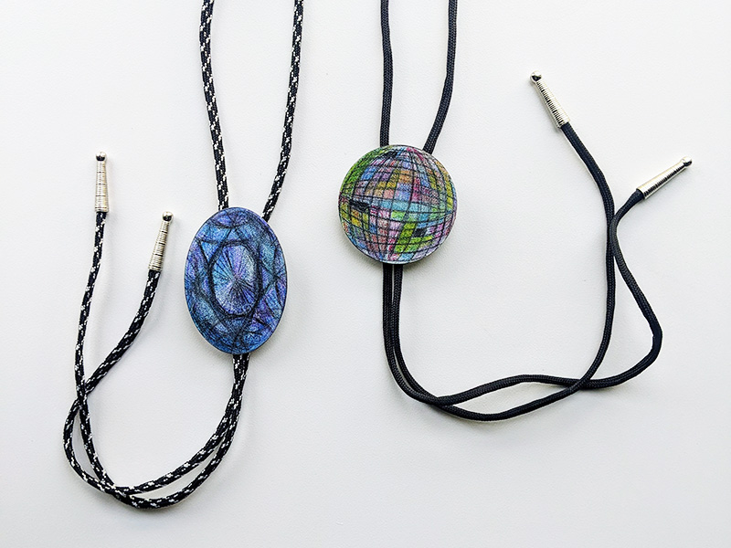 Photo of two handmade bolo ties with black strings on a white background.