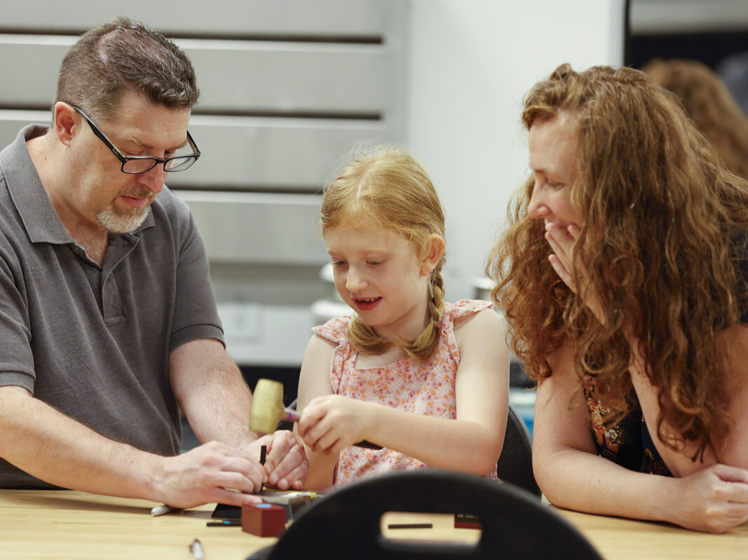 Photo of a man, woman, and young girl working on a metal art project in an art studio at the Windgate Art School