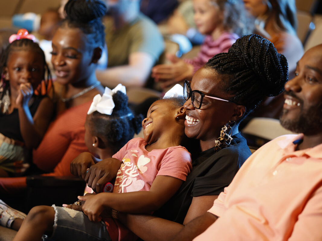 Photo of parents and children seated in a theater and smiling.