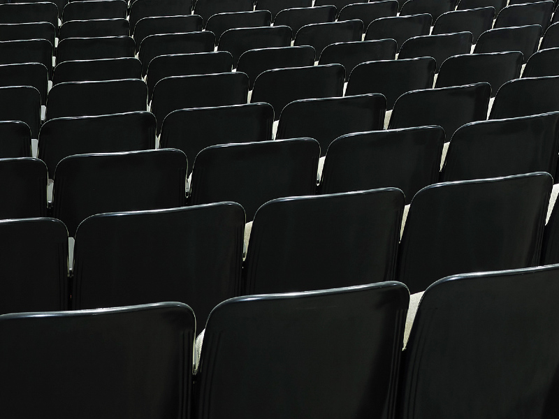 Photo of the backside of a several rows of black theater seats.