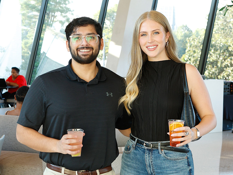 Photo of a man and woman smiling and posing while holding cocktails.