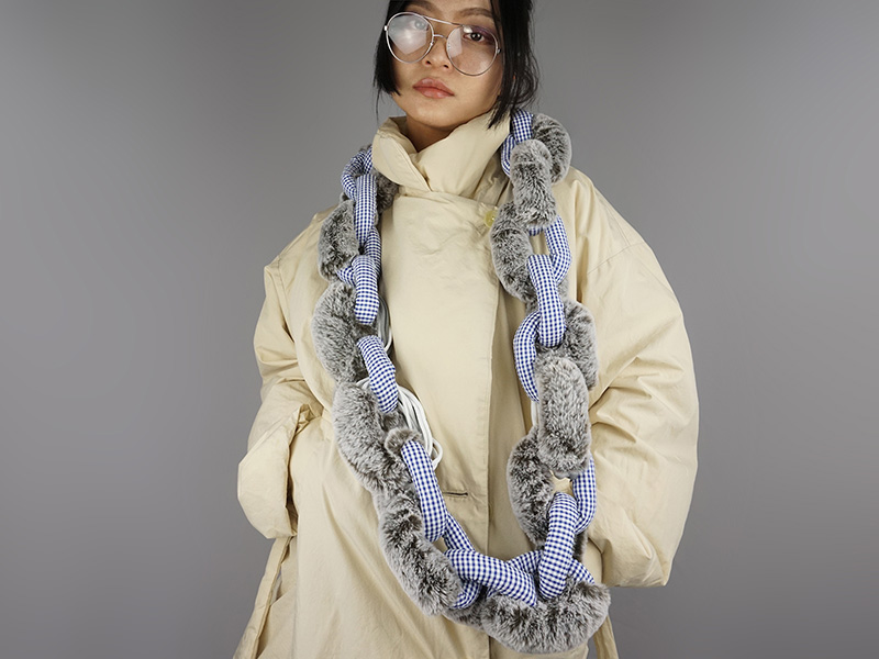 Photo of artist Dongyi Wu wearing an off-white winter jacket and handmade oversized fabric necklace.