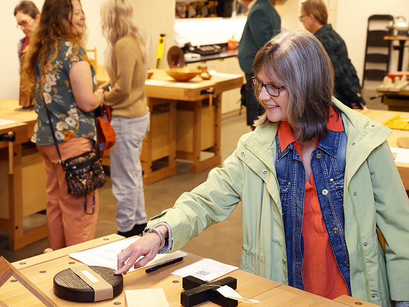 Photo of a woman looking at handmade wooden objects on a table in a wood shop at the Arkansas Museum of Fine Arts.