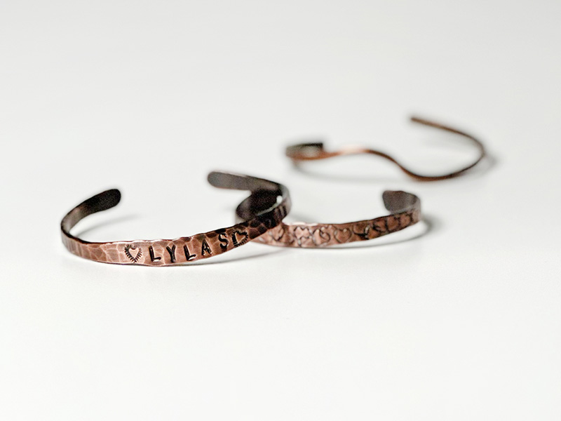 Photo of three hand-hammered copper bracelets with symbols and letters stamped into them.