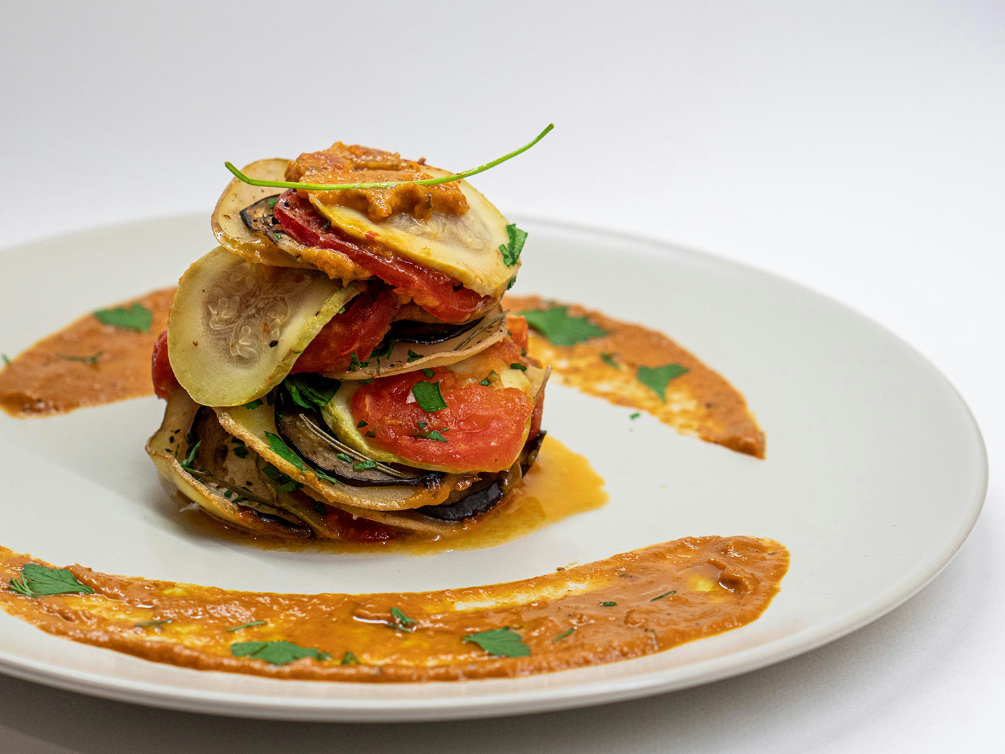 Photo of a dish of ratatouille on a white plate on a white background.