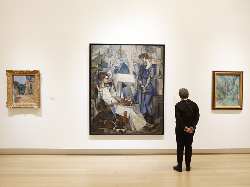 Photo of a man looking at a large Cubist painting of two women in an art gallery.