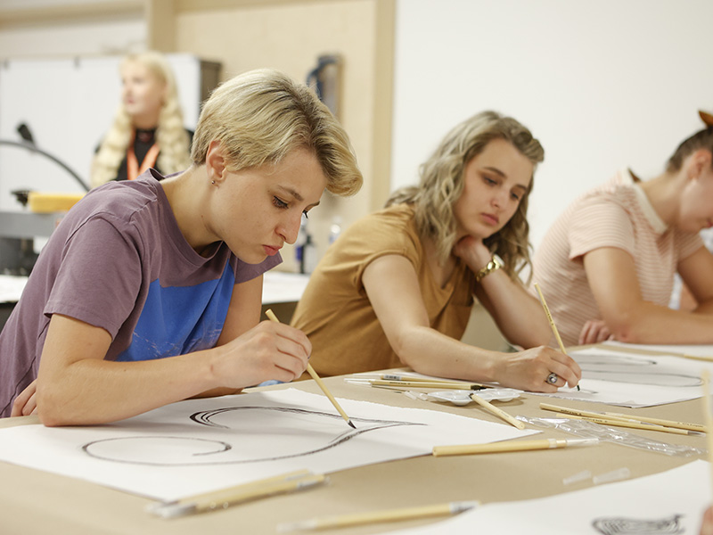 Photo of two young women painting at a table in an art studio.