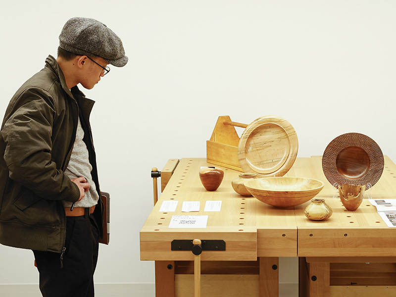 Photo of a man looking at handmade wooden vases and bowls on a table.