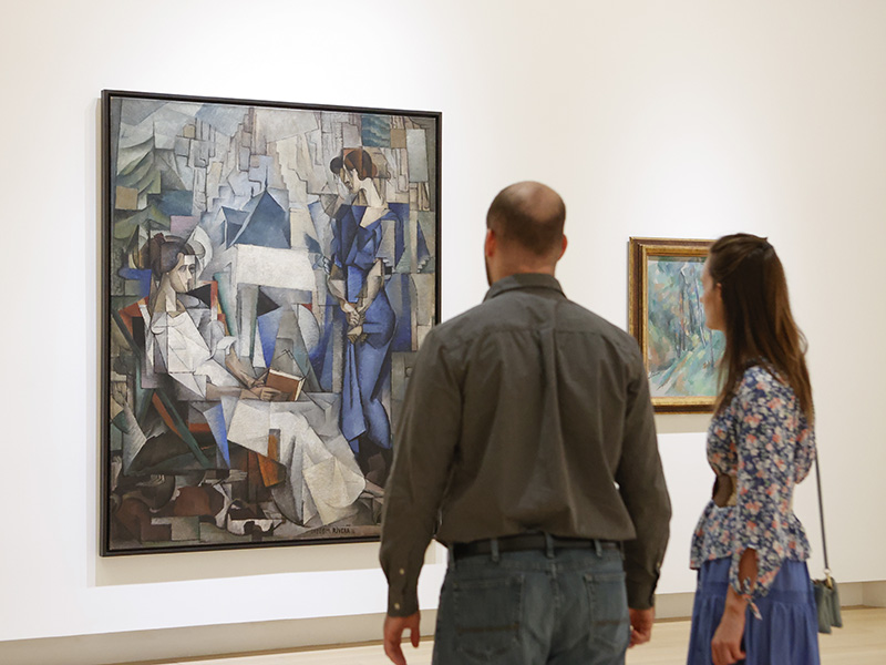 Photo of a man and a woman looking at a large Cubist painting of two women in an art gallery.