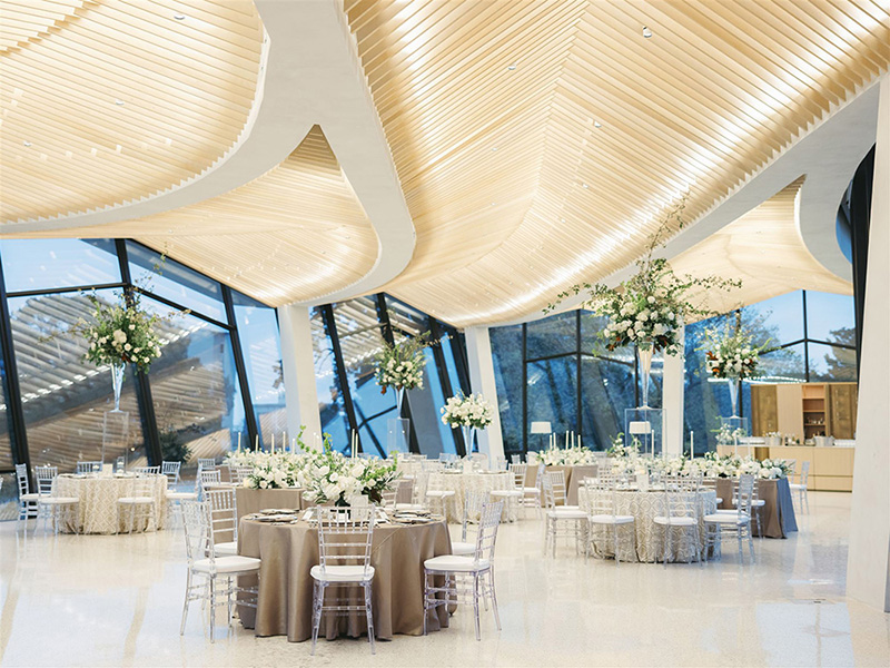 Photo of the Cultural Living Room at AMFA decorated with several dining tables surrounded by chairs with large flower arrangements.