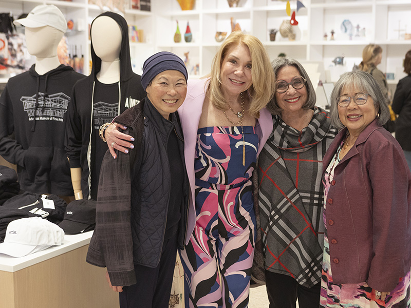 Photo of four women smiling and posing together in the AMFA Museum Store next to a display of mannequins wearing black AMFA hoodies.