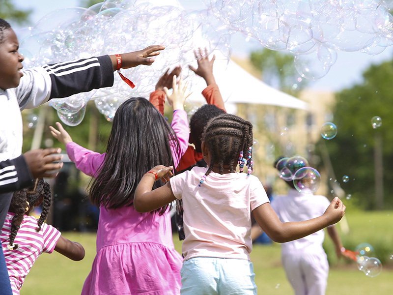 Photo of several children running with their hands up in the air while large bubbles float above their heads.