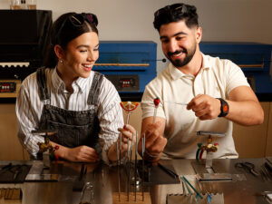 Photo of a man and a woman in an art studio inspecting small glass pieces on rods.