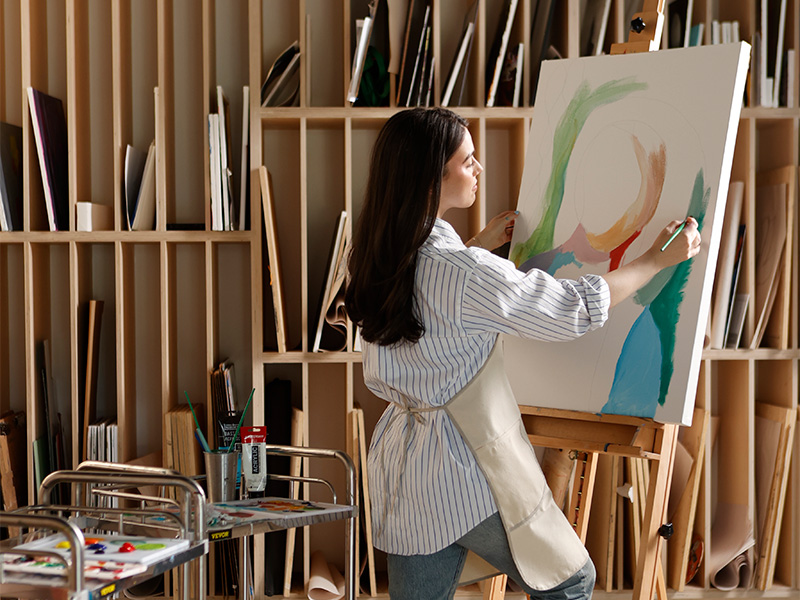 Photo of a woman standing and painting on canvas at an art easel.