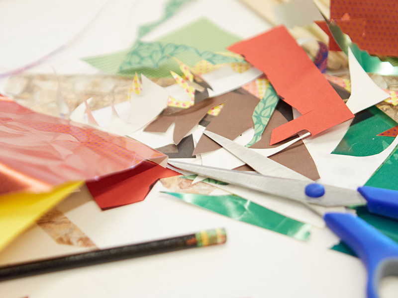 Close up photo of scissors, a pencil, and scrap pieces of paper sitting on a table.