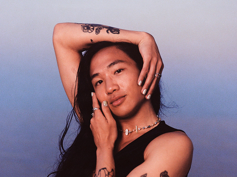 Photo of a person with long dark hair posed with their hands on their face.