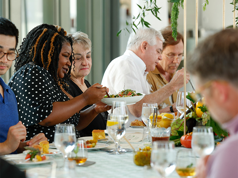 Photo of people sitting at a table and passing plates of food to each other.