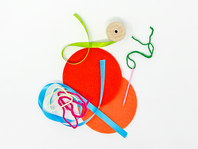 Photo of two felt circles, three strings of yarn, and two curls of ribbon lying on a white tabletop.