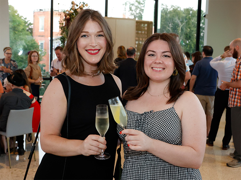 Photo of two women posed smiling and holding cocktails at a party.