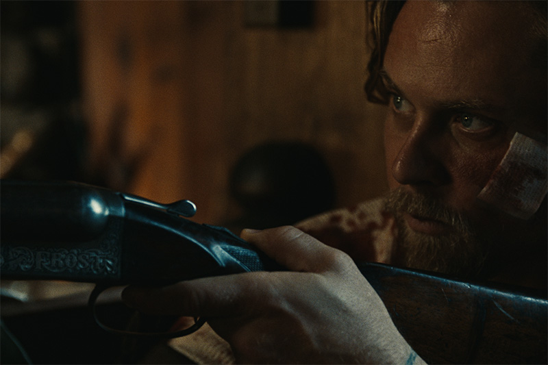 Film still from the movie Violet Ends showing a close up of a man with a bandaged face holding a rifle.